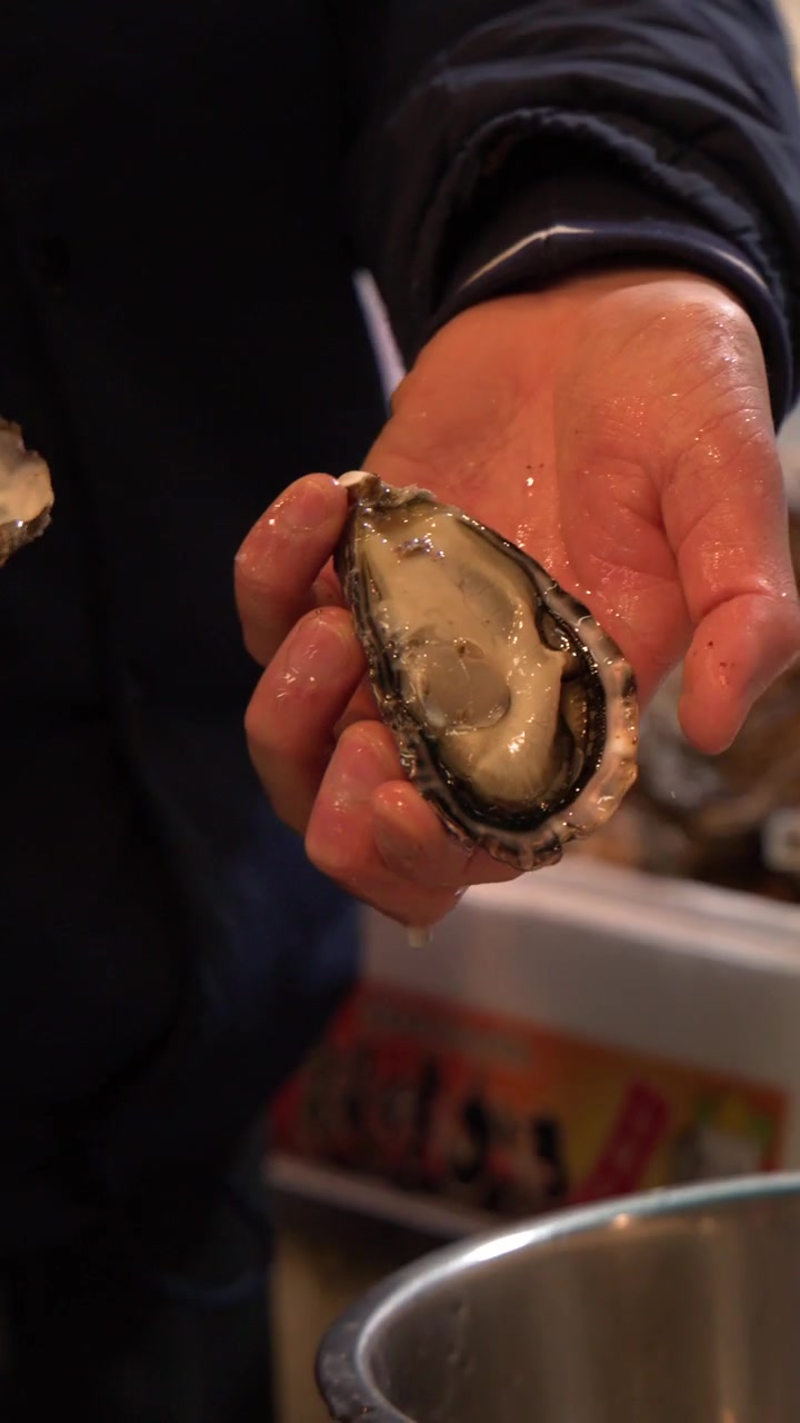 Close-up shot of a worker skillfully opening a fresh oyster with a shucking knife