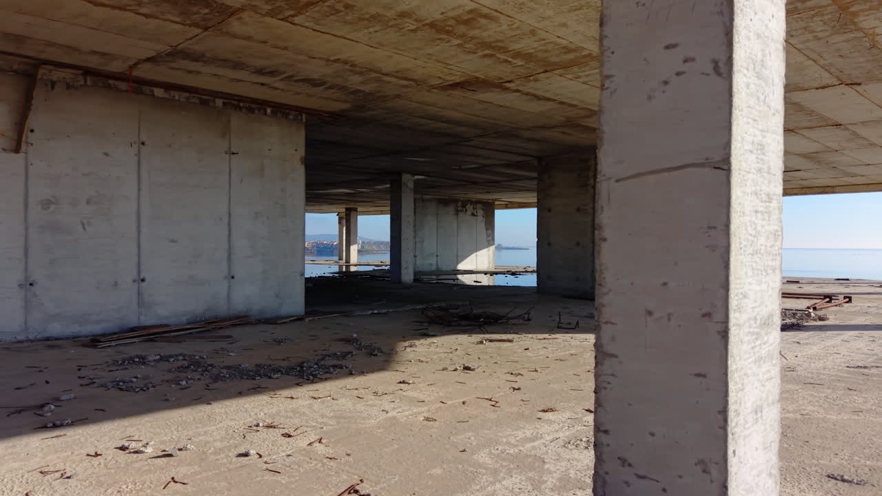 Vista interior de paredes y suelos de hormigón en bruto con el océano visible a través de grandes aberturas de ventanas. Interior de un edificio de hormigón sin terminar. Aérea.