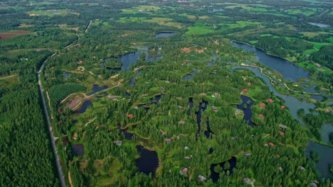 Drone-view-of-the-lush-green-eco-village-Amatciems-in-Latvia,-surrounded-by-forest,-lakes-and-streams