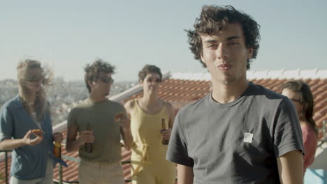 portrait of a young caucasian man looking at the camera and eating pizza while having a rooftop party with friends