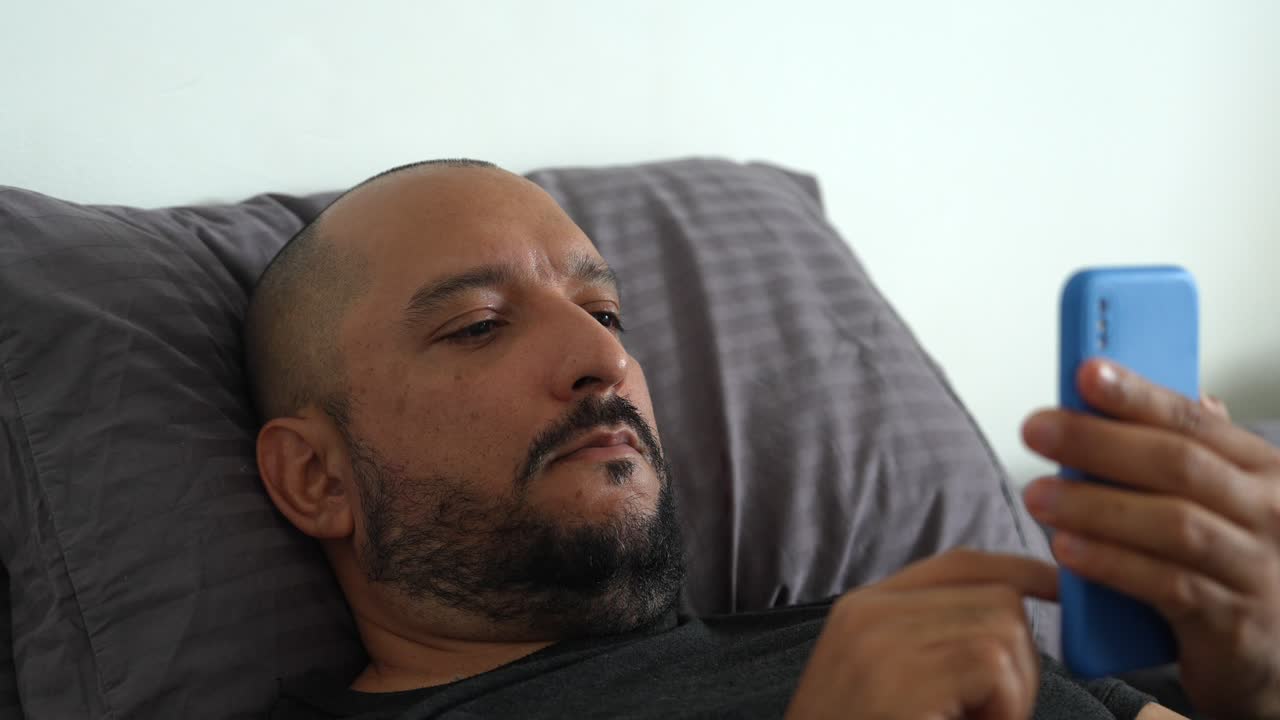 Hispanic Man in His 40s Lying in Bed and Scrolling Social Network on Smartphone