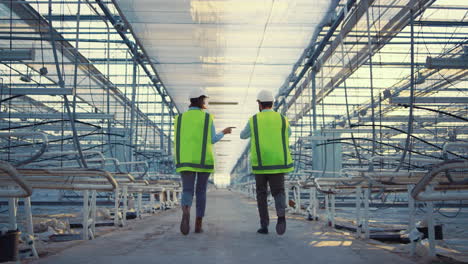 Two-factory-employees-walking-in-empty-greenhouse-discussing-production-level