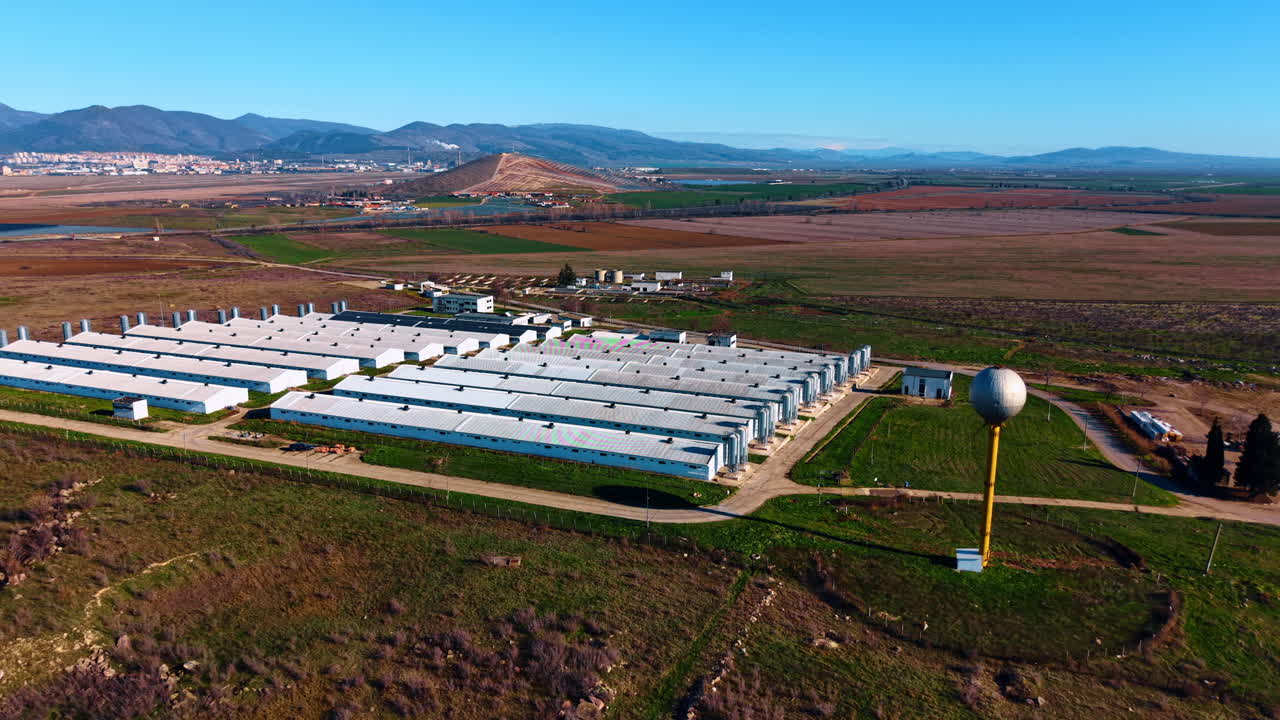 Vista aerea di una struttura agricola industriale e torre dell'acqua. Grande complesso di lunghi edifici agricoli bianchi e una torre dell'acqua sferica in un paesaggio di pianura rurale