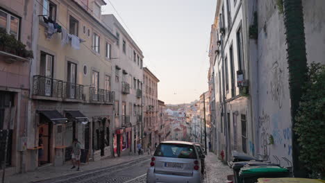 wide static shot of city streets as people stroll along the gorgeous historic cobblestone streets during a golden hour sunset in lisbon, portugal.