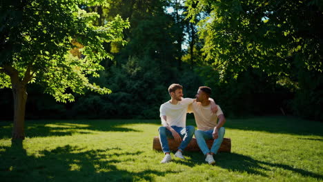 two men sitting on a log in a sunny park