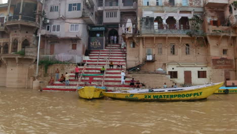 Cinematográfica-Cámara-Lenta-Escaleras-A-Varanasi-India-Crucero-Por-El-Río-Ganges-Barcos-Del-Canal-Reunión-Del-Estado-Del-Norte-Antigua-Ciudad-Santa-Provincia-De-Ghat-Pradesh-Paisaje-Gris-Tarde-Nublada-Fangosa-Marrón-Izquierda