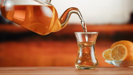 pouring lemon tea from a glass teapot into a cup