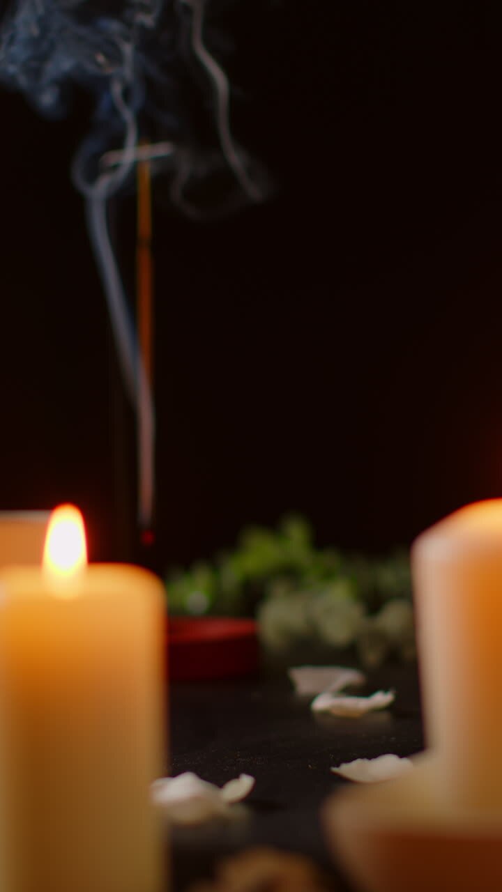 video vertical de vida fija de velas encendidas con pétalos esparcidos incienso palo contra fondo oscuro como parte de la relajante decoración del día de spa 1