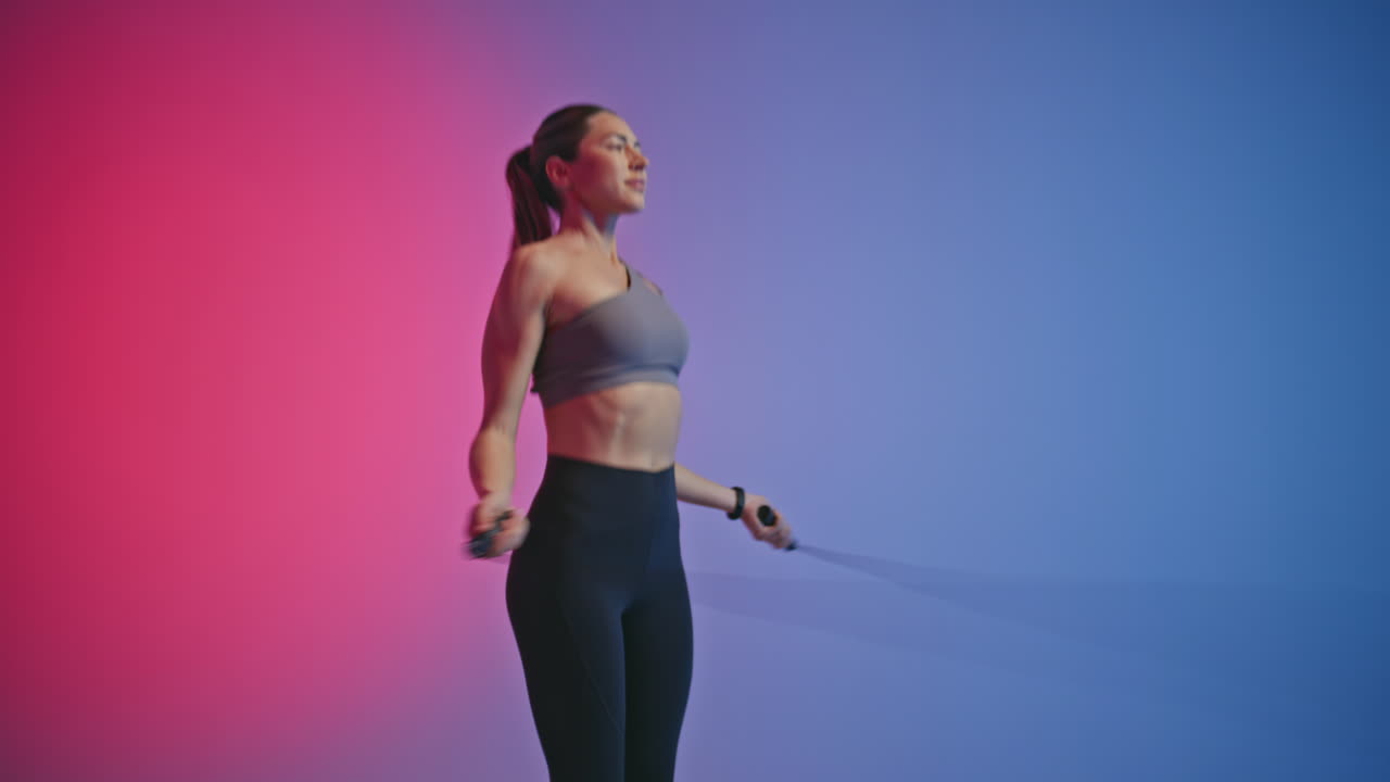Starke Frau macht Cardio-Workout mit Springseil in einem Neon-Raum. Fittes Mädchen springt