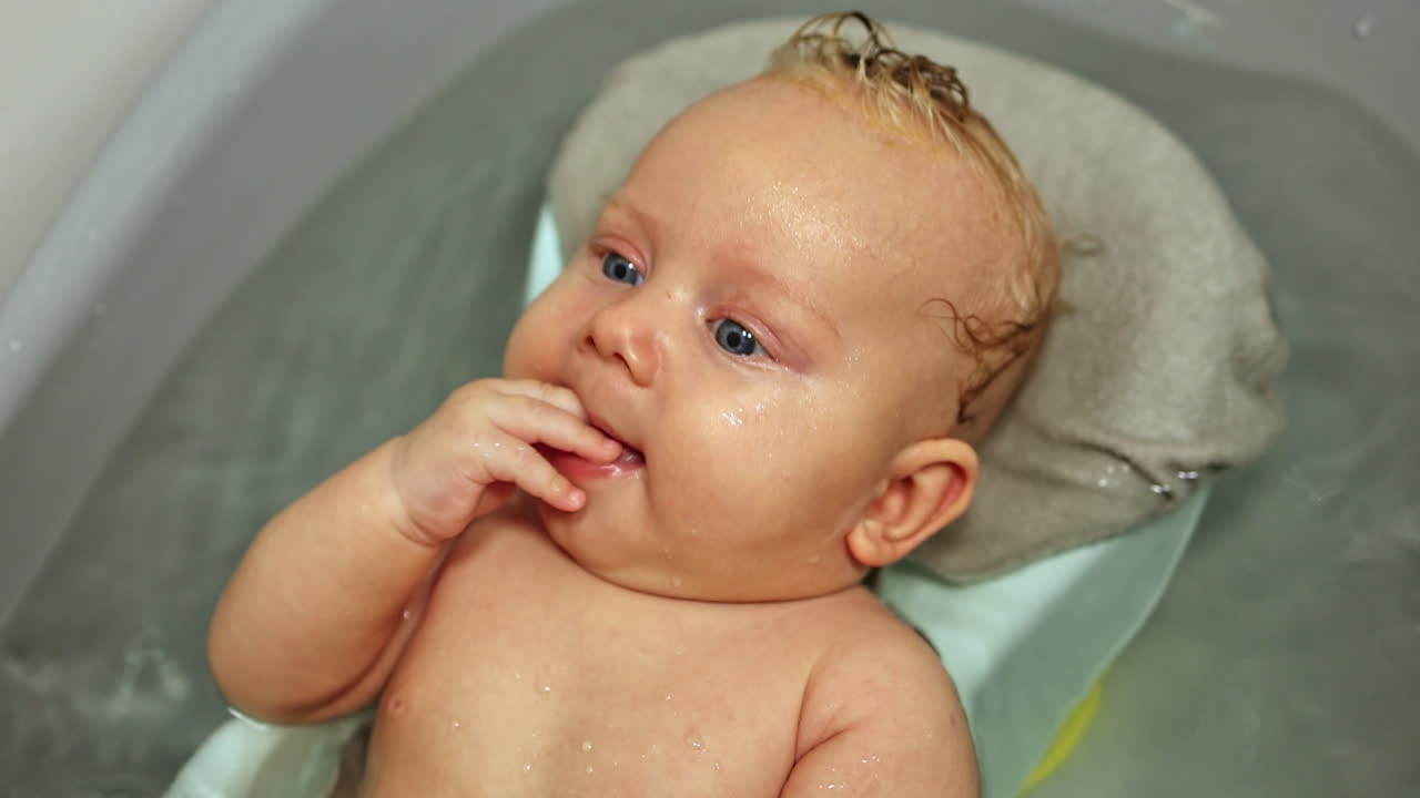 Bathing the baby in the bath while lying on the stand. Baby's first baths. Baby hygiene. A 3-month-old baby is lying in the bathroom