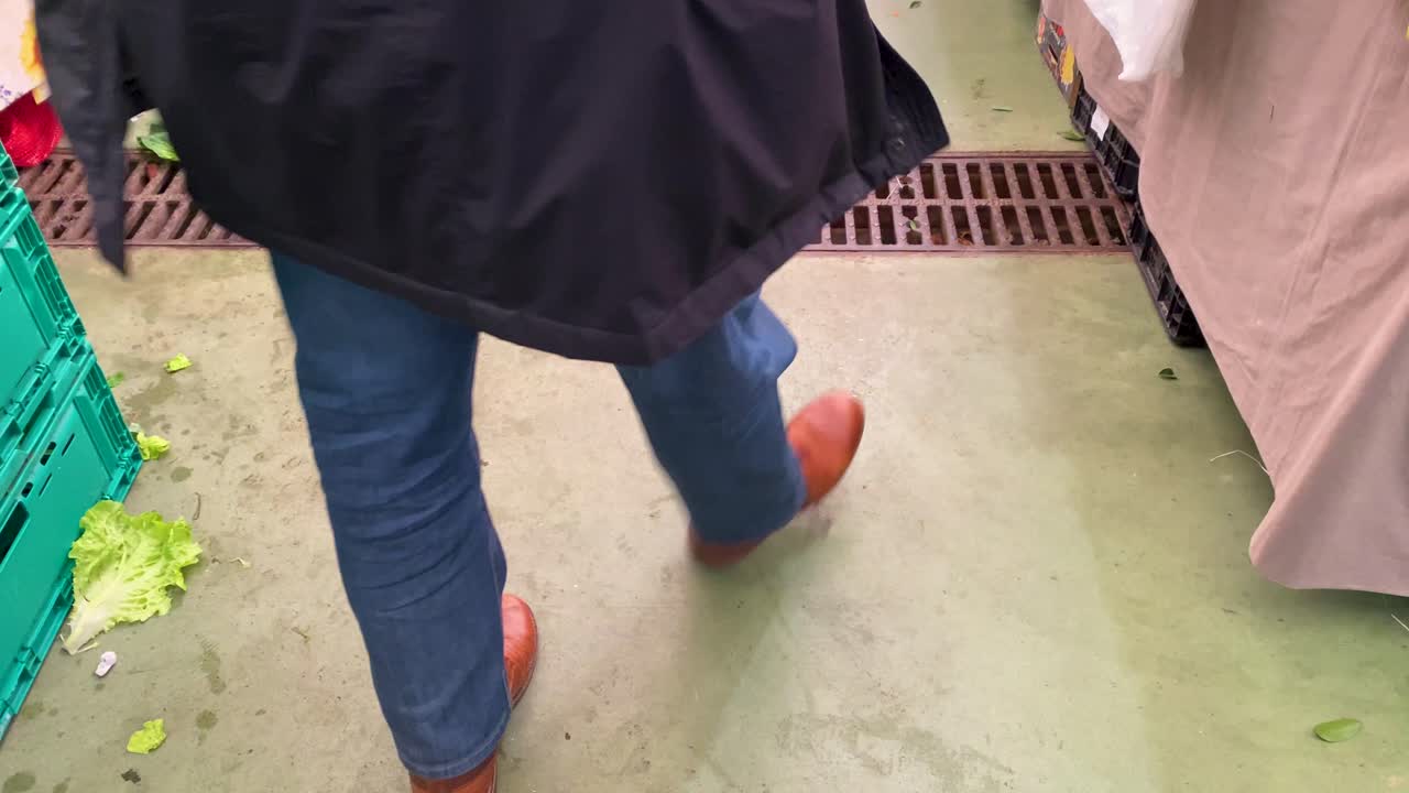 바퀴가 달린 큰 가방을 들고 신선한 농산물 시장을 걷고 있는 농산물 시장의 사람들을 허리 아래로 찍은 사진