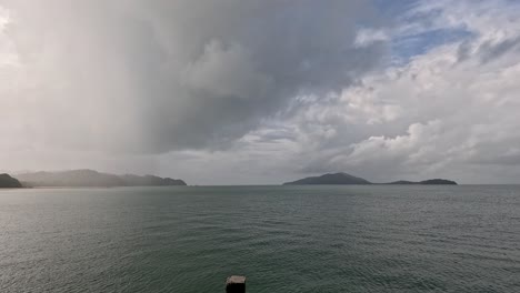 a wide shot captures a dramatic rainstorm moving across the sea toward a forested coastline on ko phayam, with shifting clouds and changing light