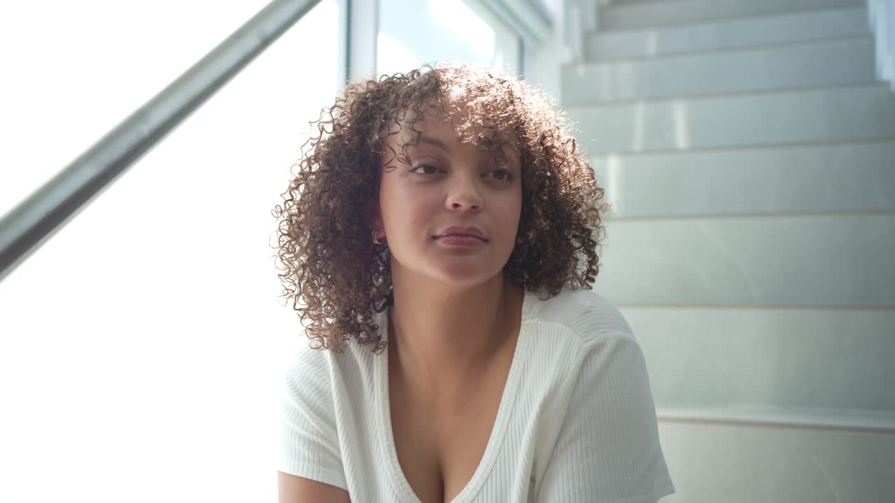 Mulher afro-americana sentada nas escadas em casa, a câmera se aproximando, sorrindo com um smartwatch.