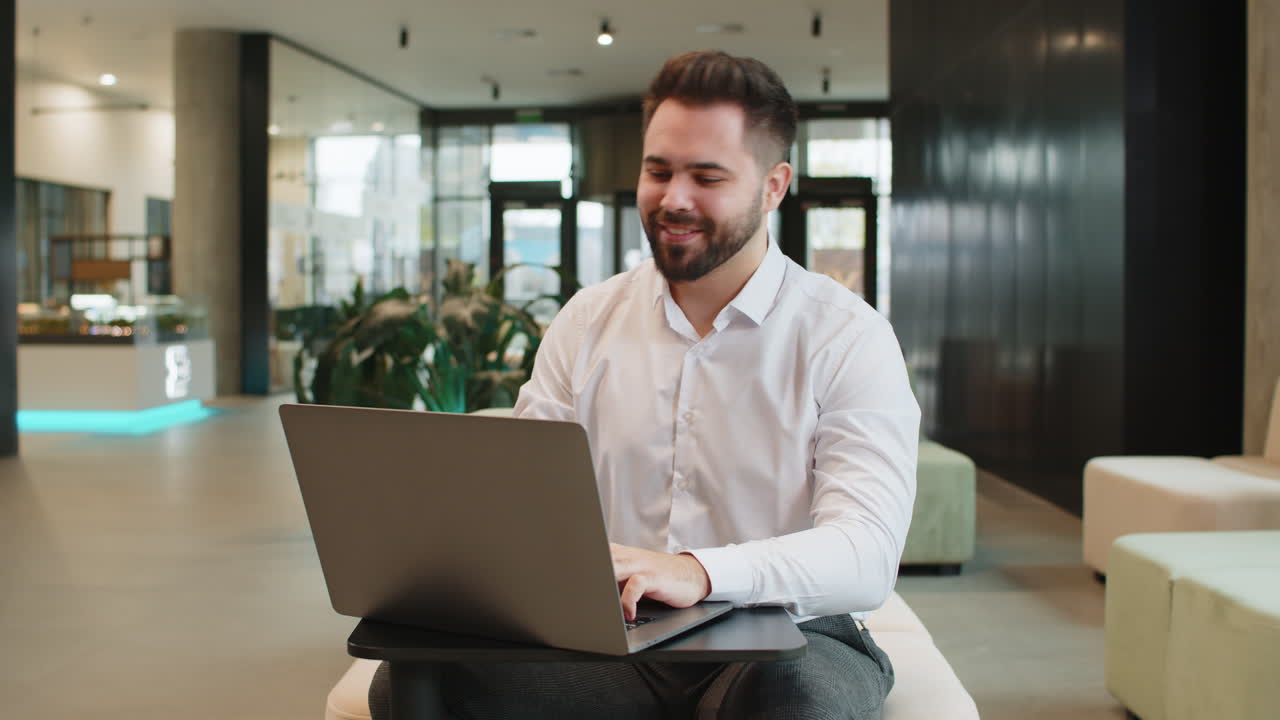 Smiling businessman closing laptop pc computer after finishing work sitting in modern office lobby