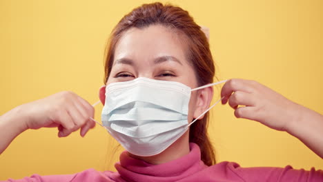 civid-19 상황이 노란색 배경으로 풀린 후 행복하고 즐거운 미소를 짓고 신선한 공기를 위해 보호 마스크를 벗고 갈색 머리의 젊은 아시아 여성을 닫습니다