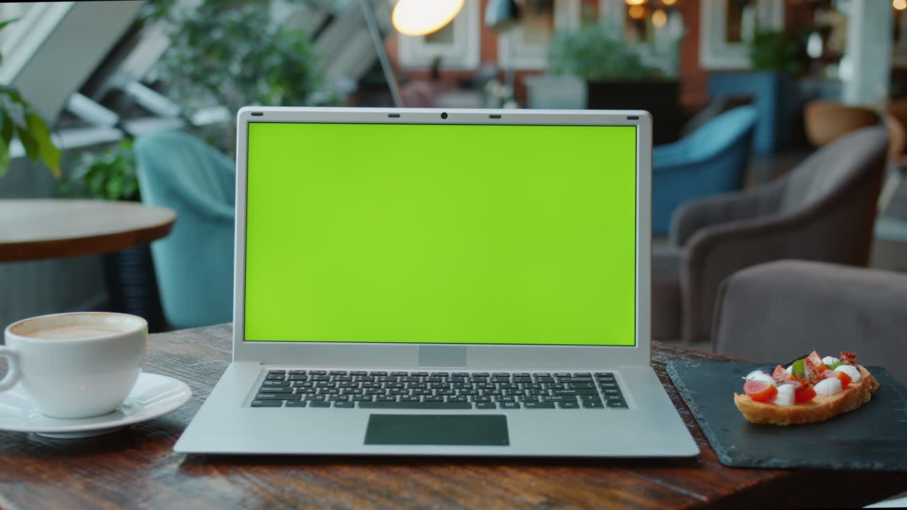 Primo piano di un moderno laptop con schermo verde chroma key su un tavolo in un caffè con cibo e bevande