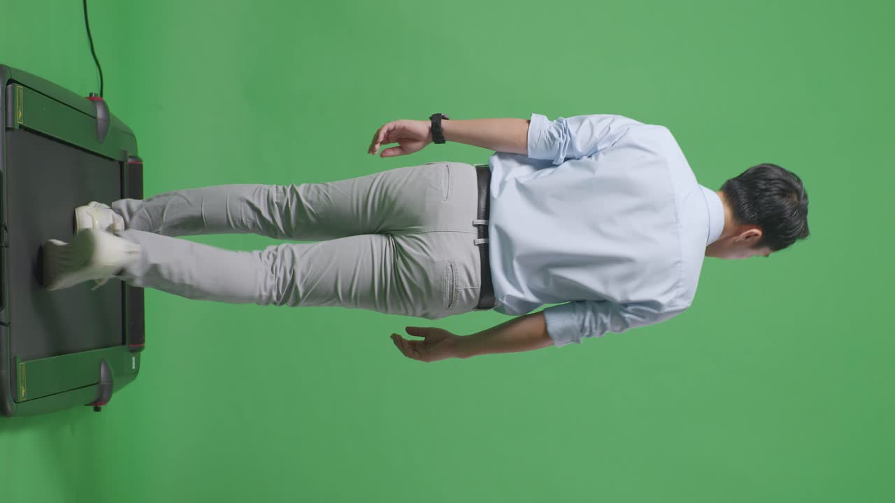 동양 사업가의 전체 몸을 뒤로 보면서 걸어서 스튜디오의 녹색 화면 배경에서 둘러보고 있습니다.