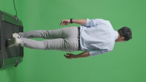 동양 사업가의 전체 몸을 뒤로 보면서 걸어서 스튜디오의 녹색 화면 배경에서 둘러보고 있습니다.