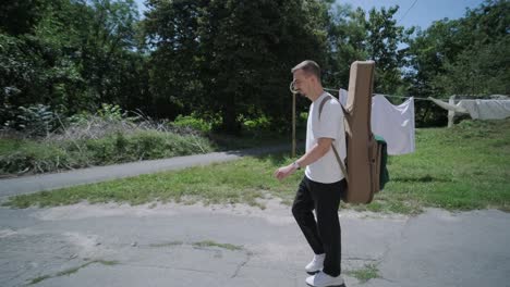 young man walking with guitar on street near forest