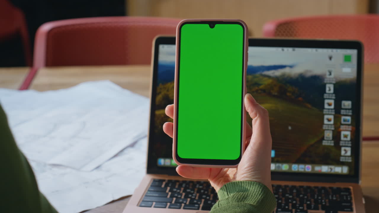 Woman watching green screen smartphone sitting work desk with laptop closeup