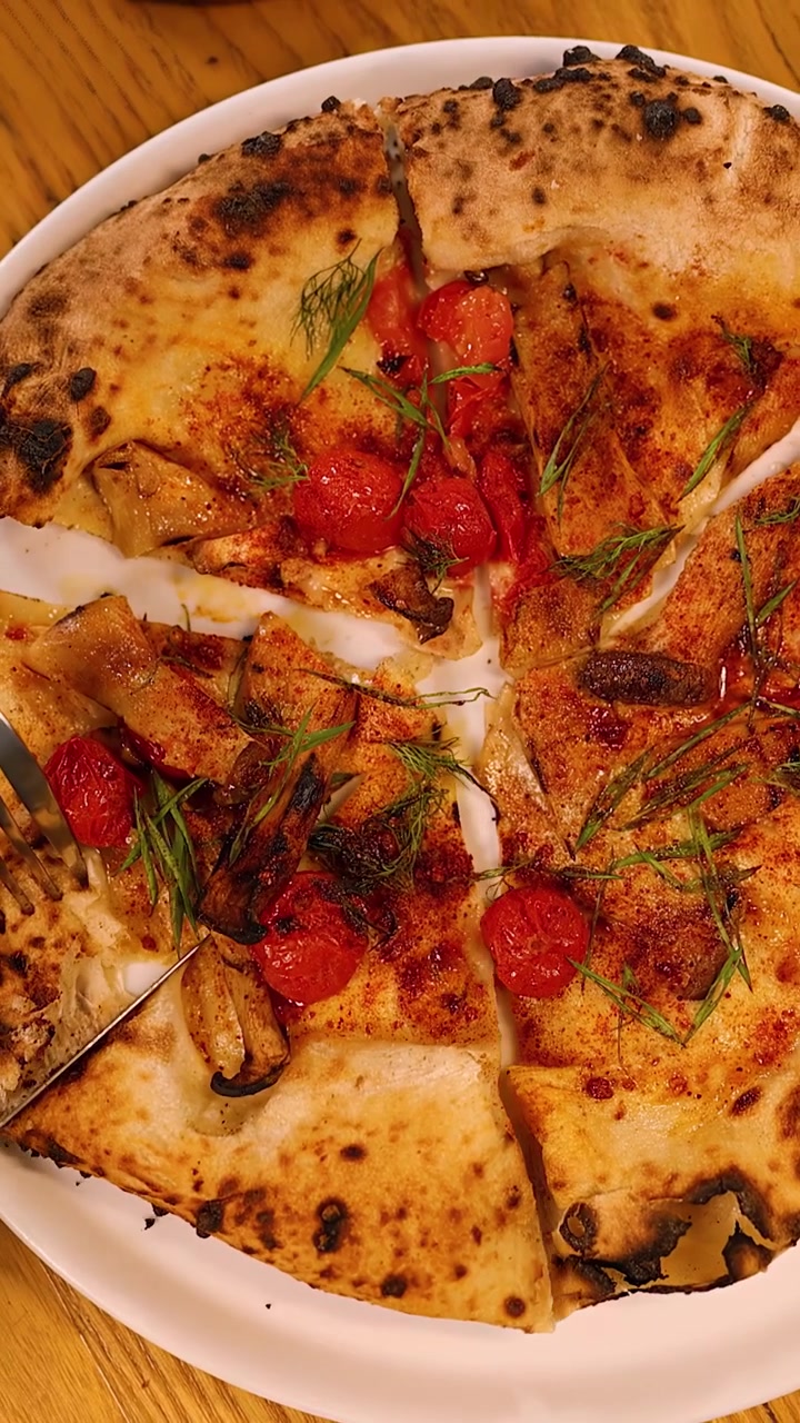 Tomada de cima para baixo de mãos usando uma faca e um garfo para fatiar pizza artesanal de tomate cereja.