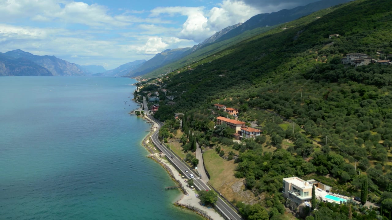 Göl kenarı yolu, dağlar ve yemyeşil bitki örtüsüyle çevrili villaların havadan görünümü.