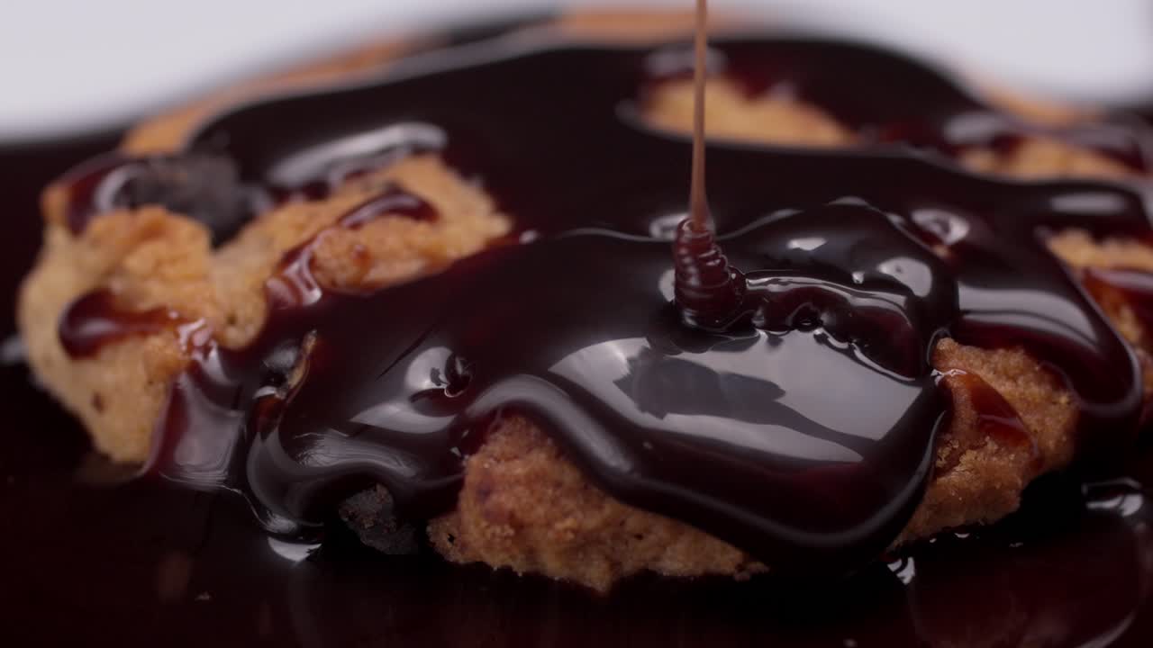 Chocolate syrup dripping over a warm cookie, creating a glossy and indulgent look