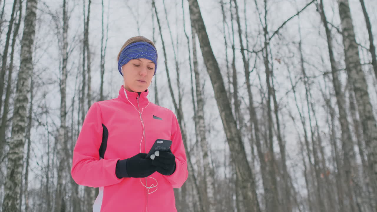 A young female on the morning jog holds in her hands a smartphone picks a music track for training. Winter run. Use modern gadgets and training applications
