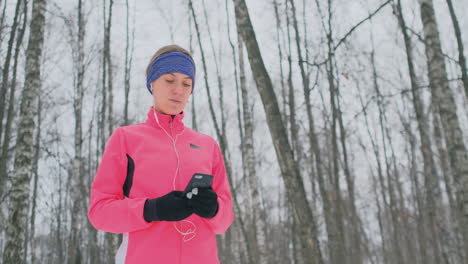 una joven que corre por la mañana sostiene en sus manos un teléfono inteligente que elige una pista de música para entrenar. carrera de invierno. utilice dispositivos y aplicaciones de formación modernos.