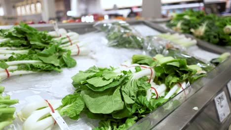 a person examines and picks bok choy from a supermarket display under bright lighting