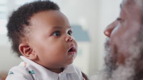 Proud-Grandfather-Cuddling-And-Playing-With-Baby-Grandson-In-Nursery-At-Home