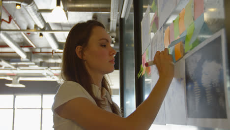 Side-view-of-young-caucasian-businesswoman-planning-and-working-on-glass-wall-of-modern-office-4k