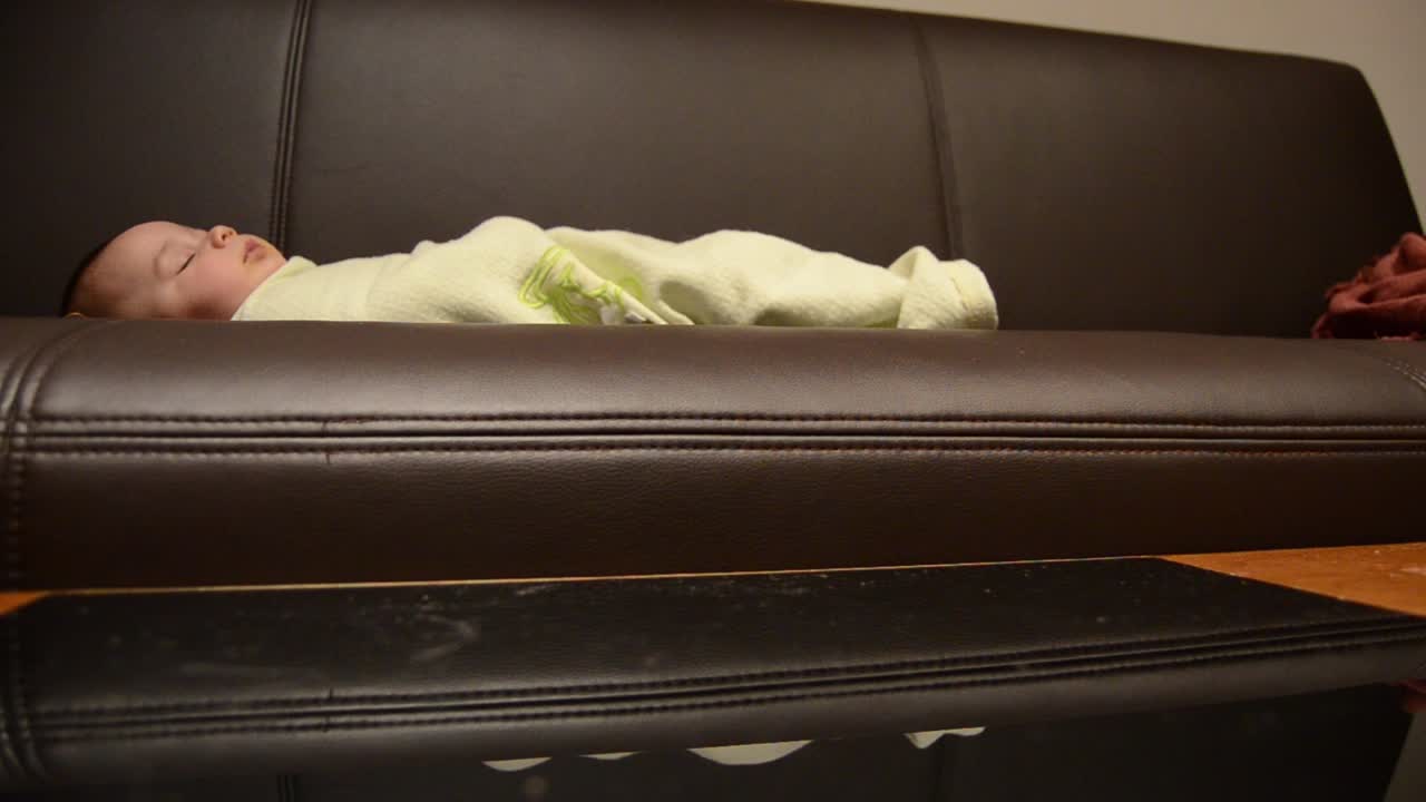 아기가 소파에서 자고 있는 동안 어머니는 커피 테이블을 청소하고 있습니다