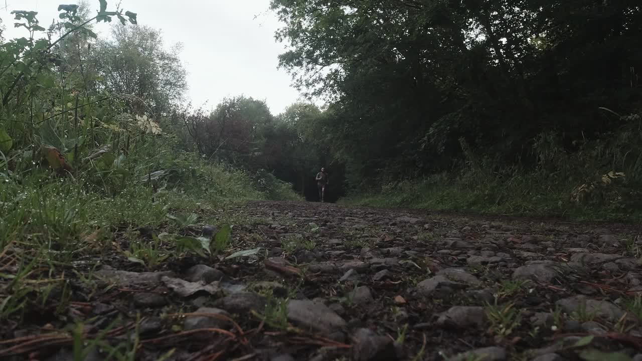 corredor corre hacia la cámara en cámara lenta con piedras y árboles