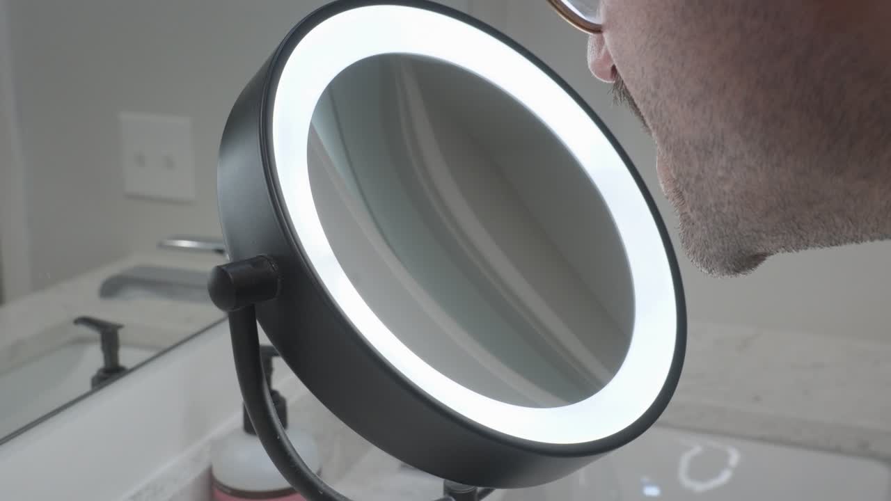 A man leans in and uses a ring light style beauty mirror