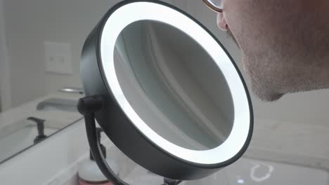a man leans in and uses a ring light style beauty mirror