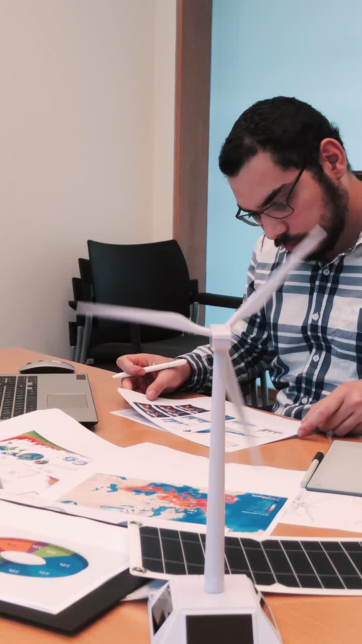 Engineer Organizing Documents, Wind Turbine Model in Foreground