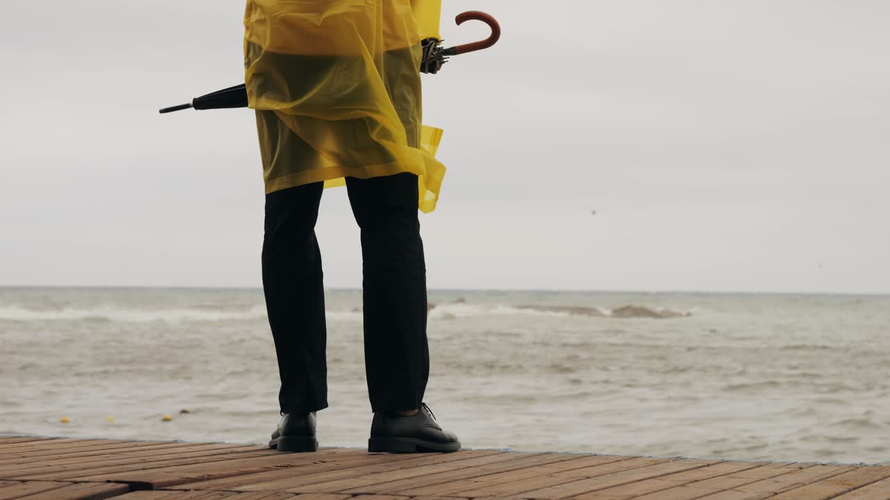 Man tourist person with umbrella and raincoat near sea ocean beach with storm on rainy european city street, lights reflecting, walking in Barcelona or Amsterdam during the rain