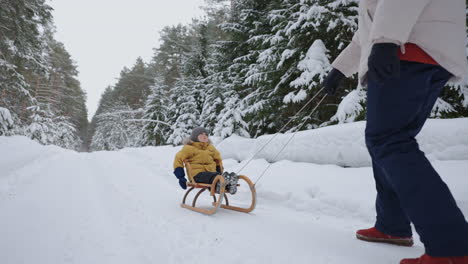 A-young-mother-and-son-have-fun-in-the-winter-in-the-forest-sledding-in-slow-motion.-happy-mom-on-a-walk-with-her-son-in-a-snowy-forest