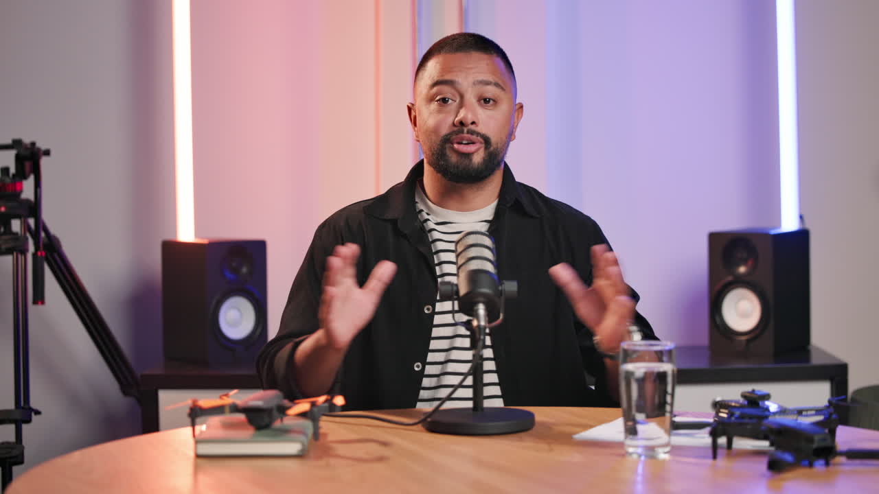 Podcast recording with man at desk with microphone, drones, and speakers