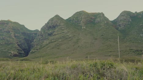 Toma-Panorámica-A-Través-De-Las-Montañas-Volcánicas-En-Kaene-Point,-Oahu,-Hawaii,-Con-Las-Llanuras-Cubiertas-De-Hierba-En-Primer-Plano.