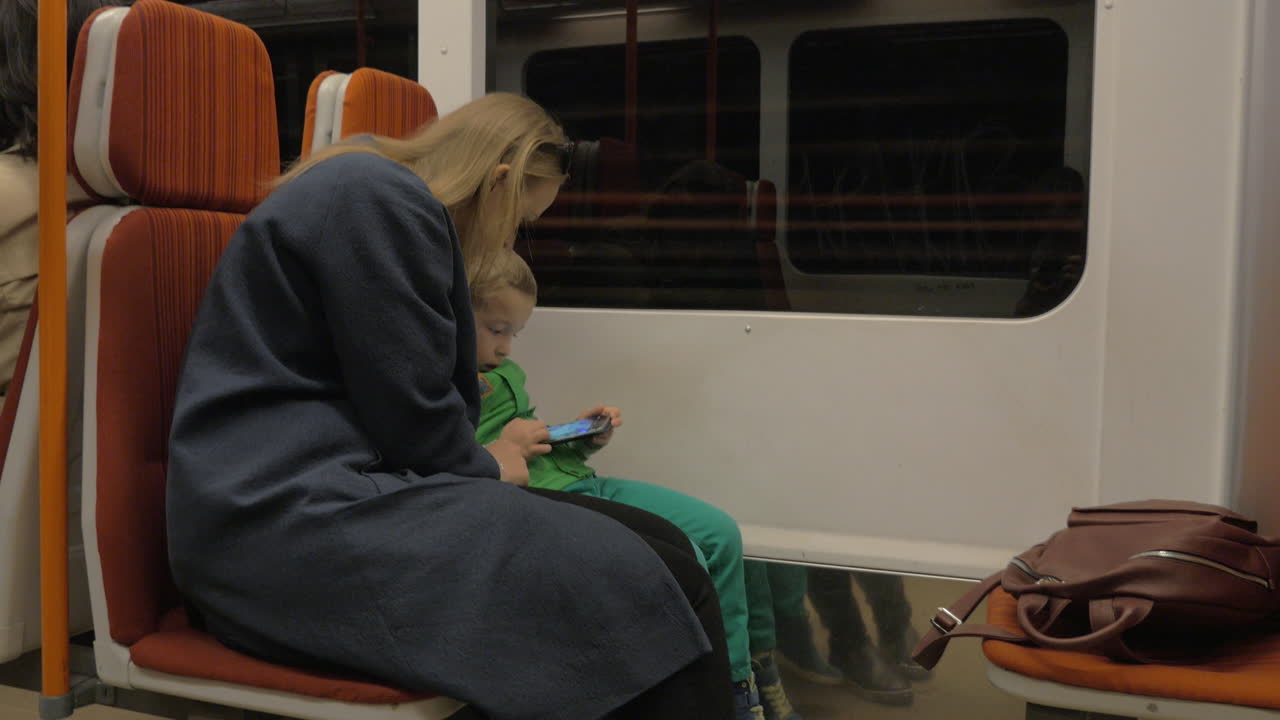 Mother and child using cell in moving subway train