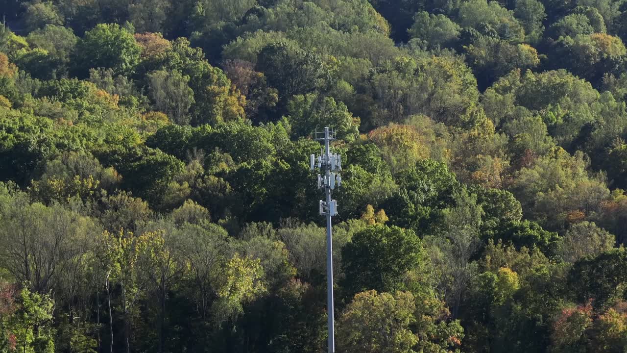 Telecommunication tower in Forest landscape of USA in autumn. Aerial orbit shot. High voltage electricity in woodland of America