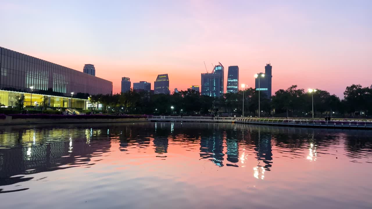 Vibrant bougainvillea frames a serene sunset over Bangkok's skyline, reflected in the tranquil waters of Benjakitti Park