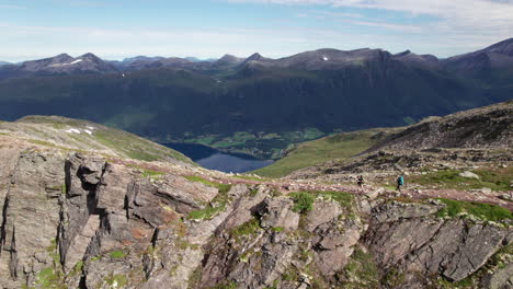 two hikers walking on the edge of a stunning breathtaking ridge in norway, romdalseggen, aerial view of a mountain landscape with a fjord in the background