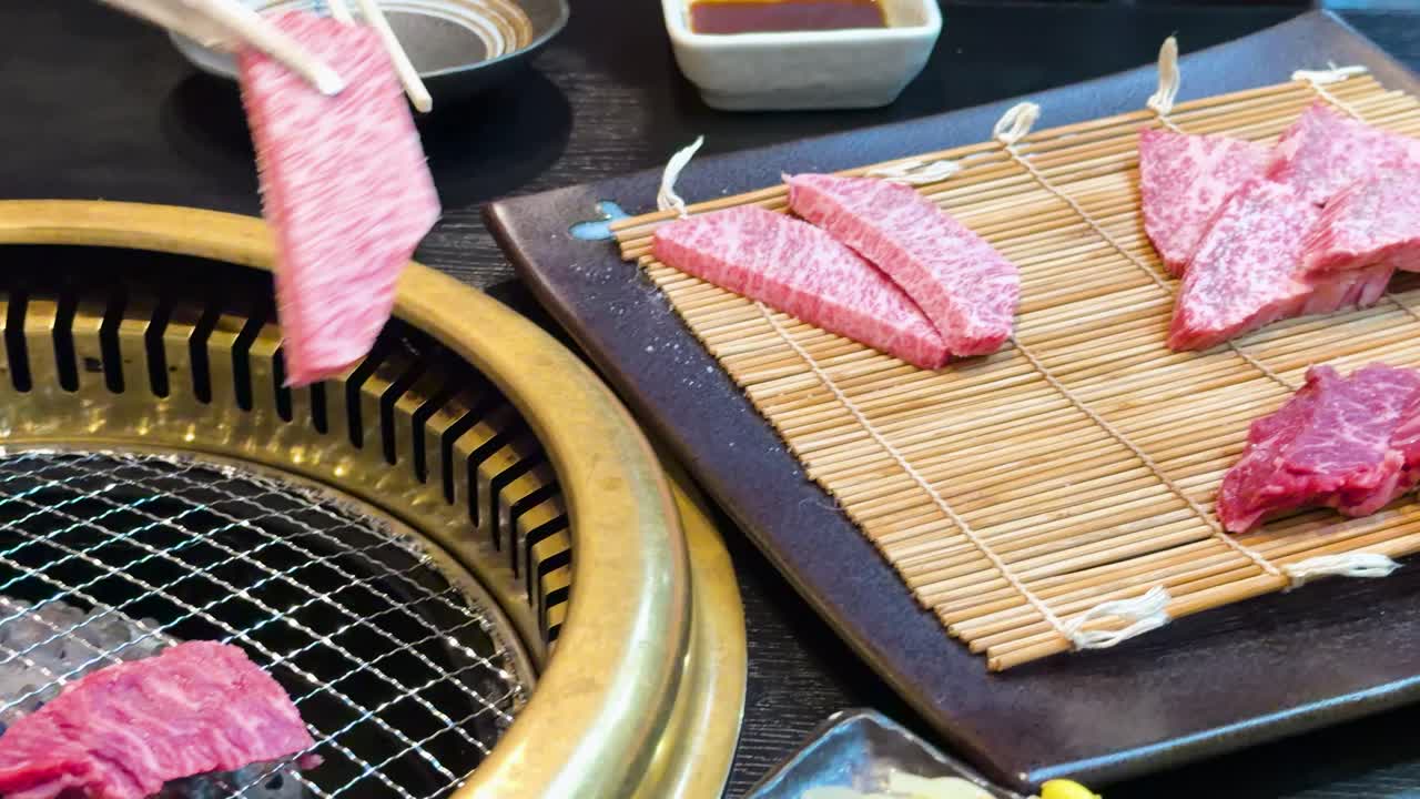 Le pinze posizionano carne di manzo Wagyu cruda marmorizzata su una griglia a carbone calda in un ristorante giapponese.