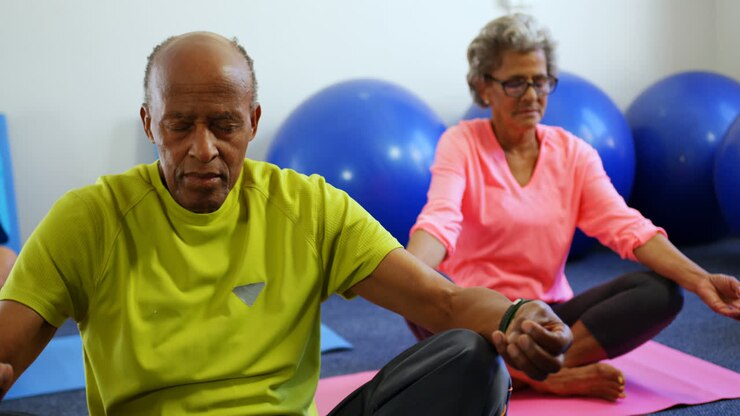 Vista frontale di anziani attivi di etnia mista che praticano yoga in una palestra 4k
