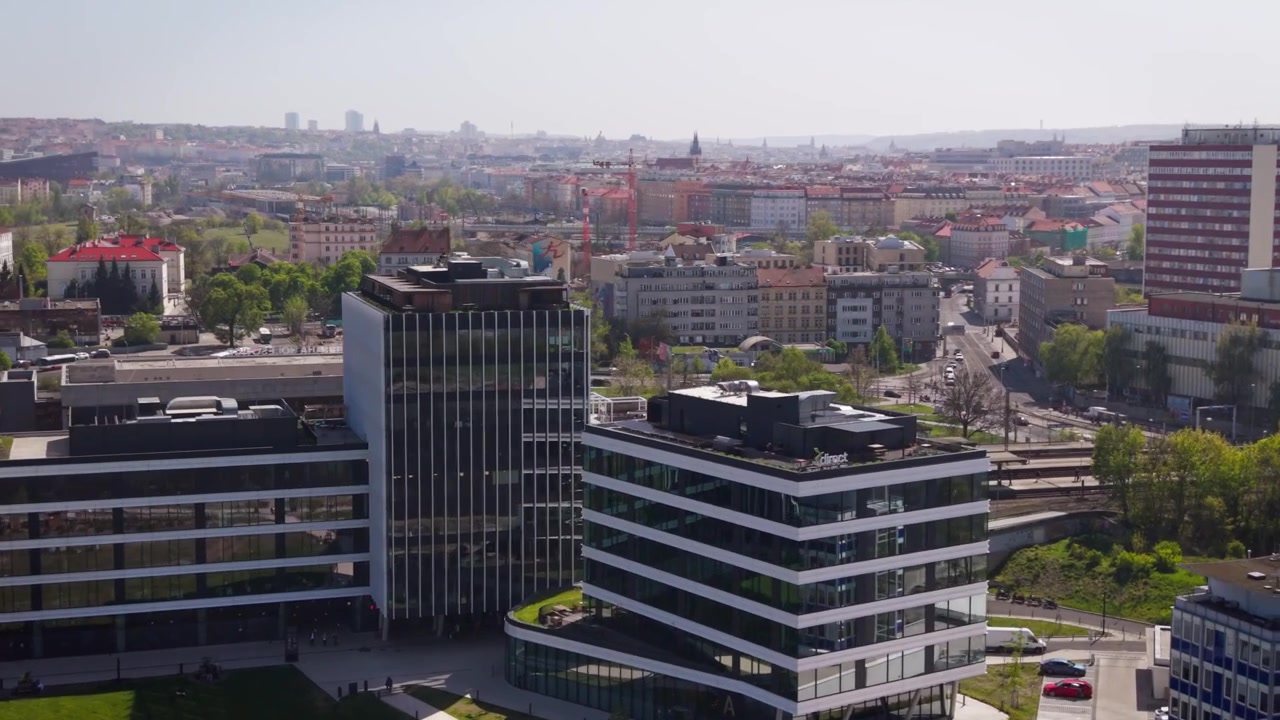 Vista aérea cinematográfica de edifícios de escritórios modernos e da área da estação de trem de Holesovice com o horizonte da cidade de Praga e a Torre Zizkov em um dia ensolarado