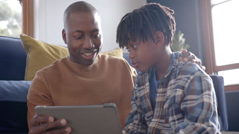 Feliz-Padre-E-Hijo-Afroamericanos-Sentados-En-El-Suelo-Y-Usando-Una-Tableta-En-Casa,-Cámara-Lenta