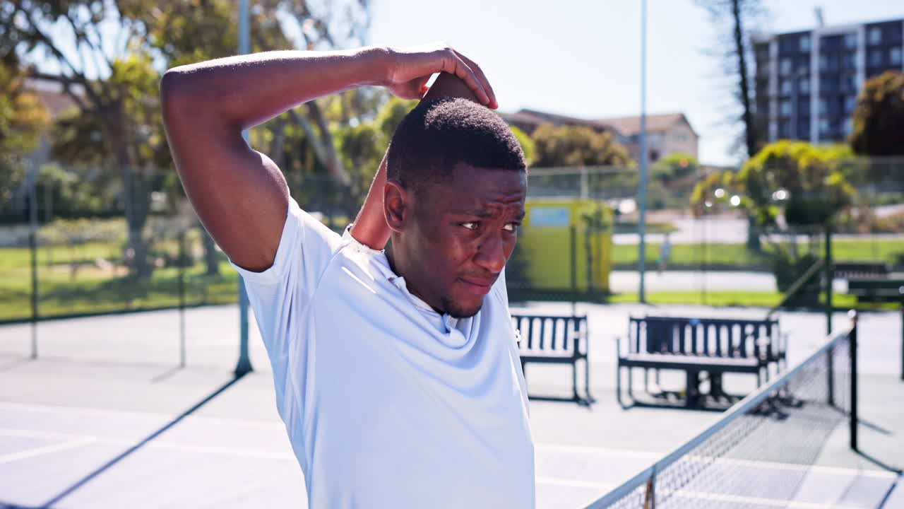 Giovane uomo di colore che allunga il braccio su un campo da tennis all'aperto
